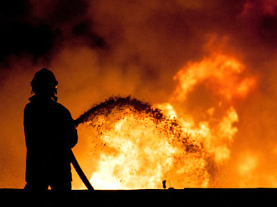 Feuerwehrmann löscht ein Feuer vor einem dramatischen, flammenden Hintergrund.