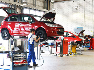 Eine Werkstatt mit roten Autos, einer wird gewartet, während Mechaniker daran arbeiten.
