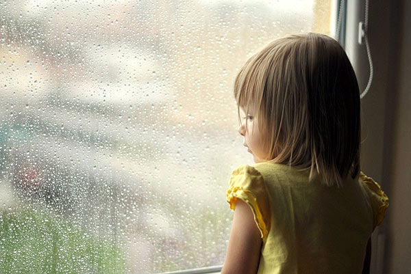 Ein kleines Mädchen steht am Fenster und schaut hinaus, während es regnet.